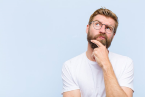 Man on baby blue background looking up and making a thinking gesture