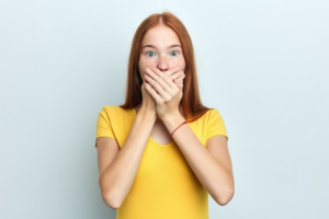 Woman on baby blue background covering her mouth to hide her lost veneer